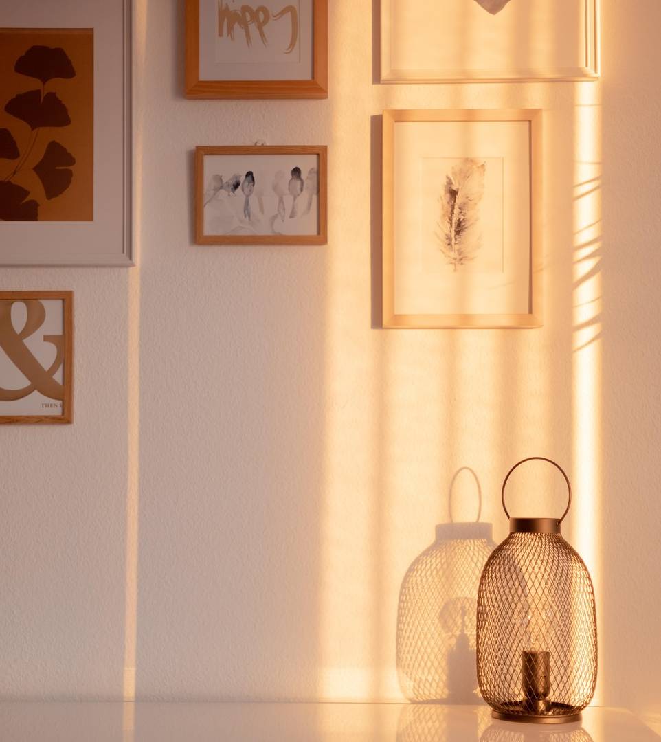 Lumière dorée de fin de journée sur un mur blanc orné de cadres, avec deux lanternes posées devant