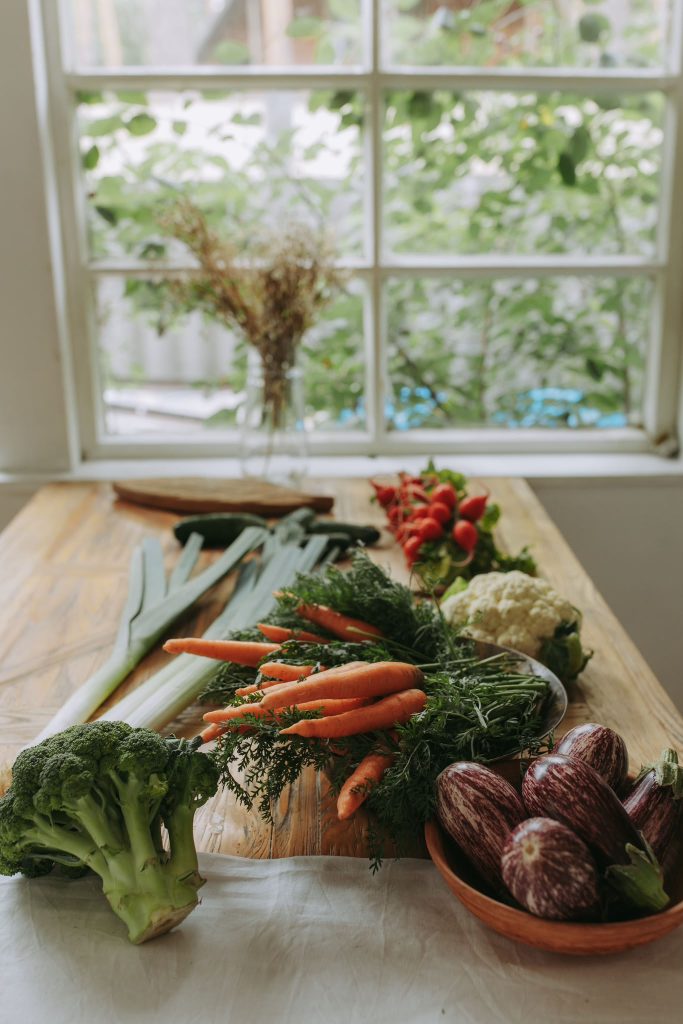 Brocolis, carottes, poireaux, aubergines et chou-fleur sur une table en bois devant une fenêtre
